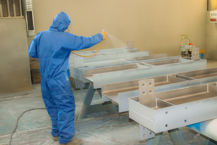 Worker spraying metal frames before coating in a factory setting in Atlanta, GA